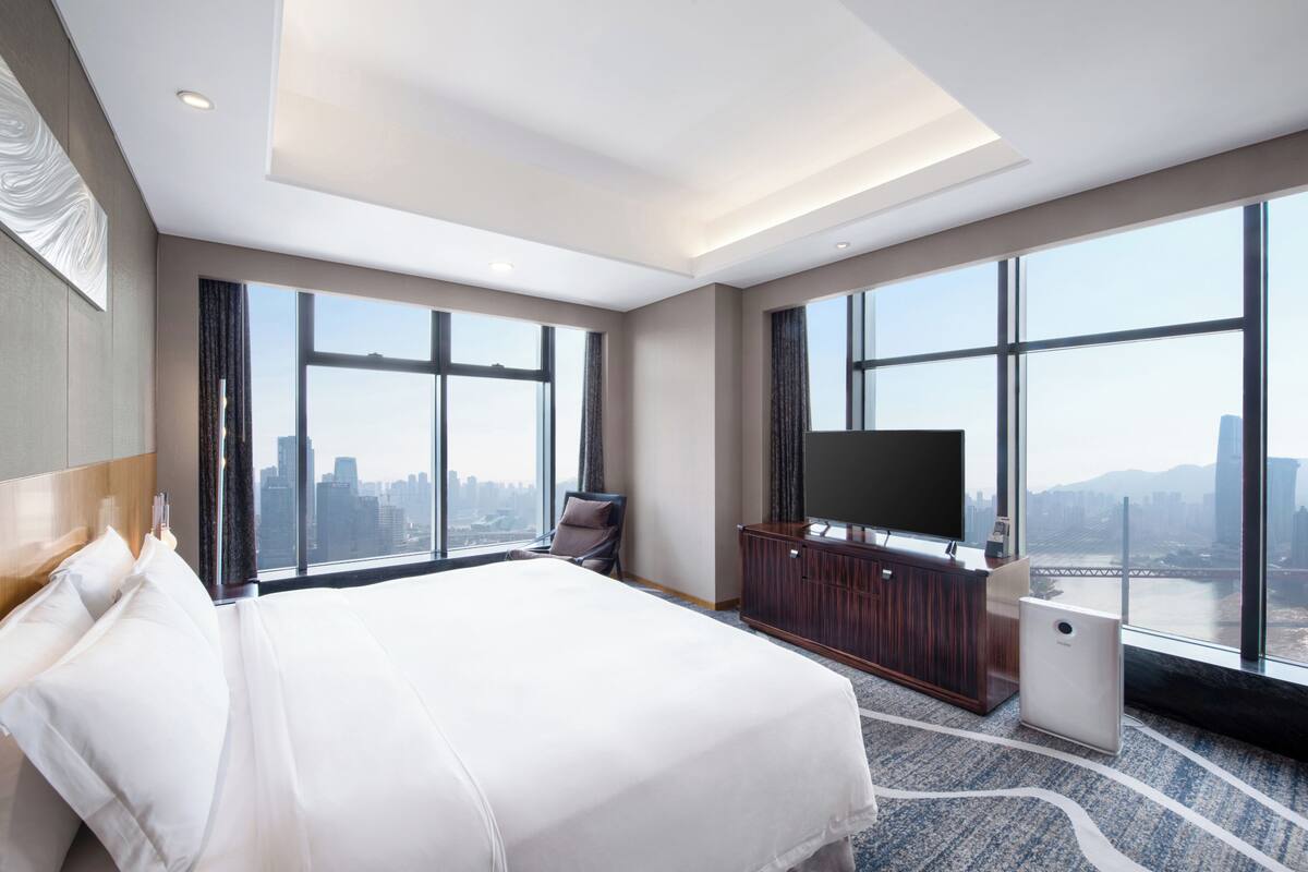 Une chambre d’hôtel avec un grand lit, une télévision, un bureau et une vue sur le paysage urbain grâce à de grandes fenêtres.