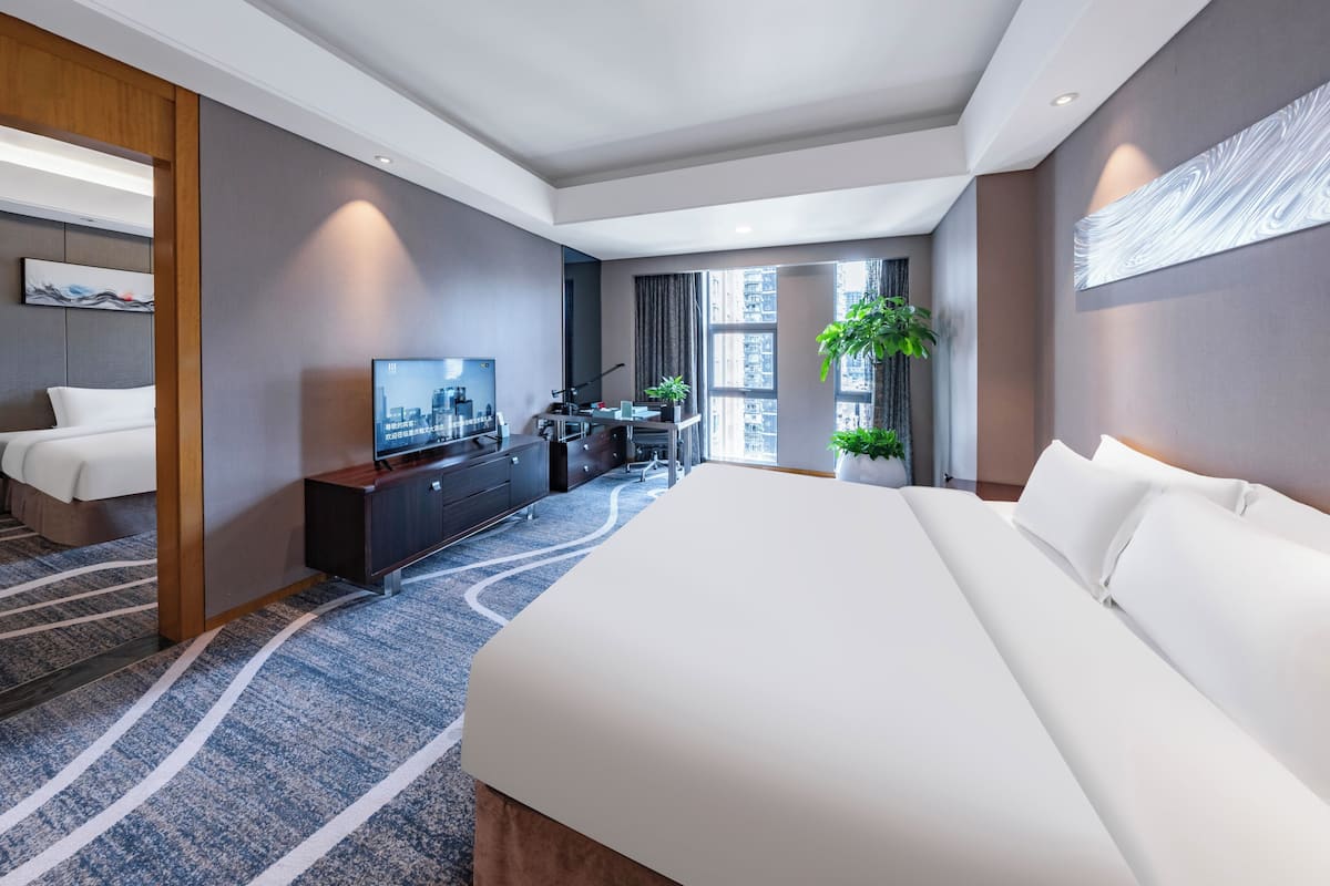 Une chambre d’hôtel moderne dotée d’un grand lit, d’un téléviseur à écran plat, d’un bureau avec un ordinateur et d’une grande fenêtre donnant sur la ville.