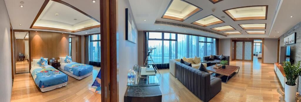 A modern hotel room with two beds, a sofa, a coffee table, and large windows offering a city view.