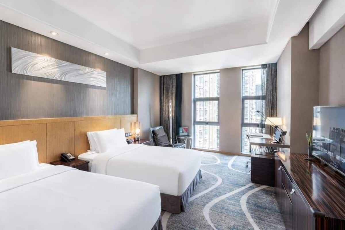 Une chambre d’hôtel avec deux lits, un bureau, une télévision et une grande fenêtre donnant sur la ville.