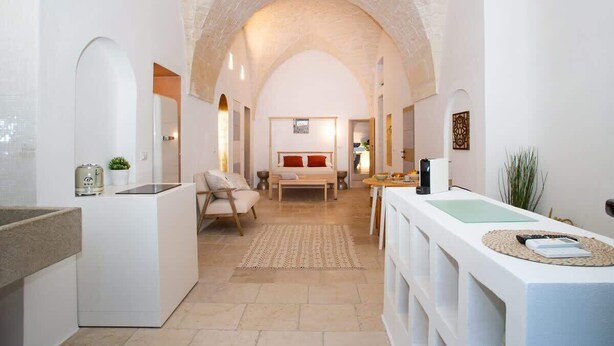 Ein modernes Interieur mit gewölbter Decke, einer Küchenzeile, einem Essbereich und einem Schlafzimmer mit Bett und Nachttisch.