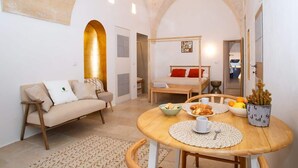 Ein gemütliches Wohnzimmer mit einer Couch, einem Esstisch mit Blumenvase und einem Bett im Hintergrund.