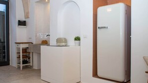 Eine kompakte Küche mit integriertem Kühlschrank, einer kleinen Arbeitsplatte und einer Holzhängeregal-Einheit.