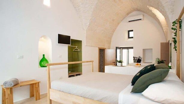 A bedroom with a wooden bed, a bench, a green bottle, and a TV on the wall. - Spring - The Fab Stay (Ostuni)