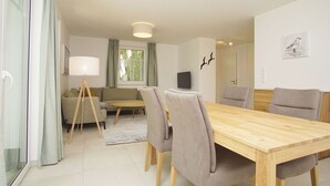 A modern living room with a wooden dining table, grey chairs, a sofa, and a floor lamp. - Beachfront apartment with terrace - Rex Rugia House 17 Apartment 01 - Beach Resort (Mönchgut)