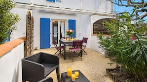 Un bâtiment blanc avec des volets bleus et une terrasse comprenant une table, des chaises et des plantes.