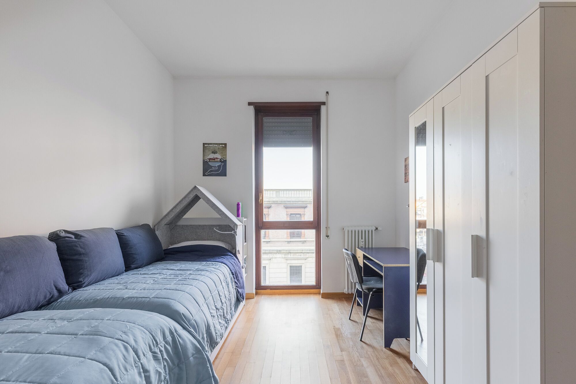 A compact bedroom with a bed, a desk, and a radiator.