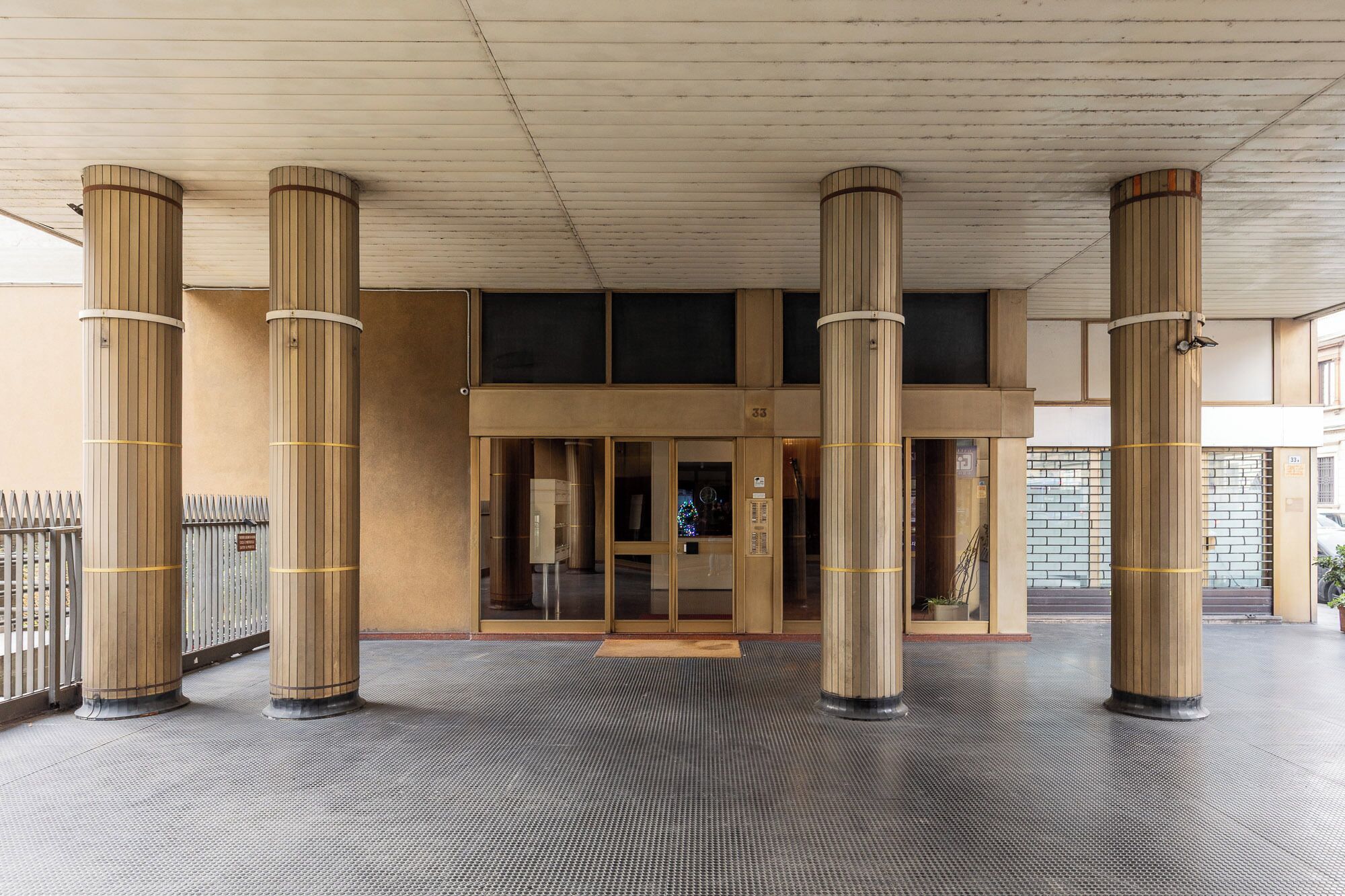 A building entrance with a covered area, large columns, and a textured floor.