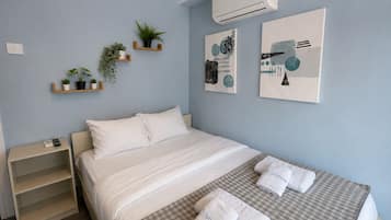 Habitación de hotel con cama, mesita de noche, estante con plantas y una obra de arte en la pared.