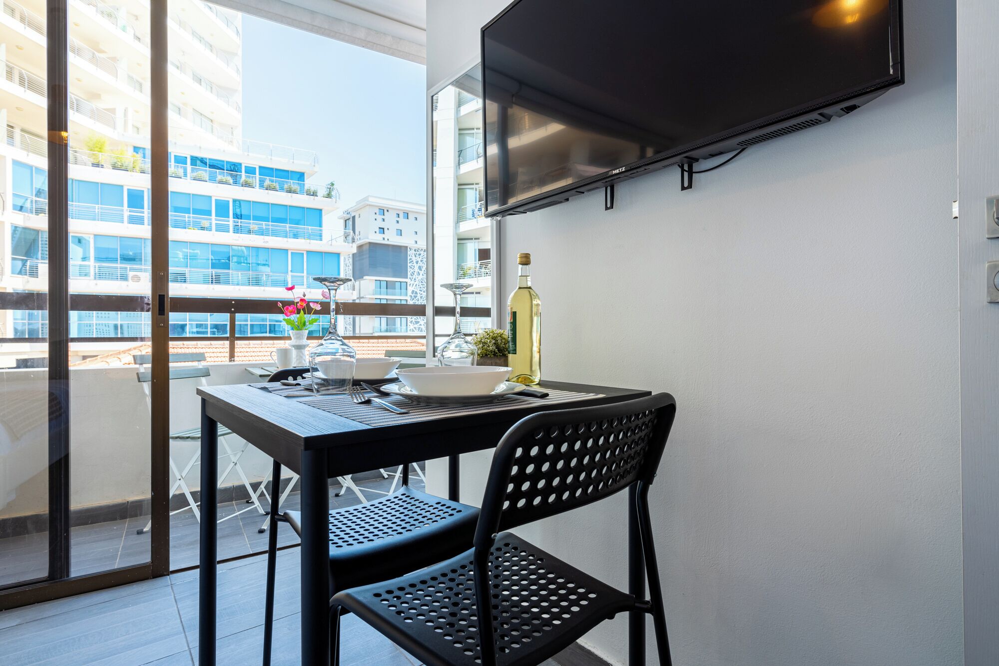 Un balcon avec une table, des chaises, une bouteille et un téléviseur.