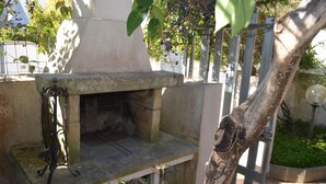 Zona de parrilla exterior con chimenea, rodeada por un muro de piedra y un árbol.