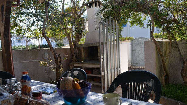 Mesa al aire libre con mantel a cuadros, un bol de pan, una botella de zumo de naranja y una taza.