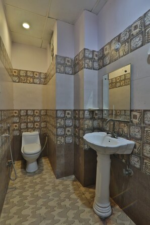 A bathroom with patterned tiles, a toilet, and a pedestal sink. - Hotel Shubhangi Inn (Lucknow)