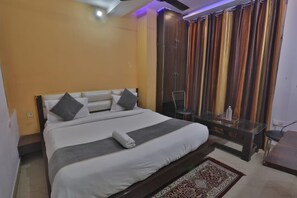 A hotel room with a bed, a glass table, a wardrobe, and a curtain. - Hotel Shubhangi Inn (Lucknow)