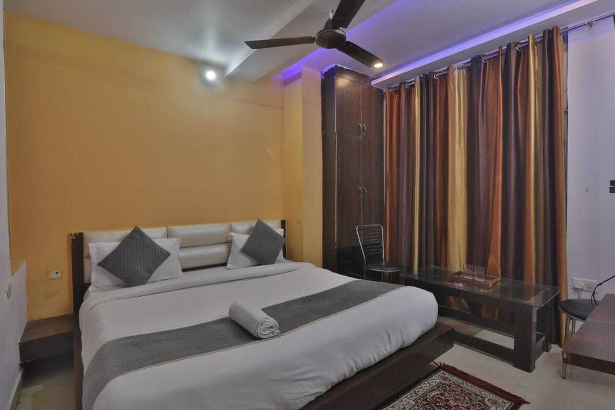 Un dormitorio con una cama, ventilador de techo, una mesa de vidrio y cortinas.