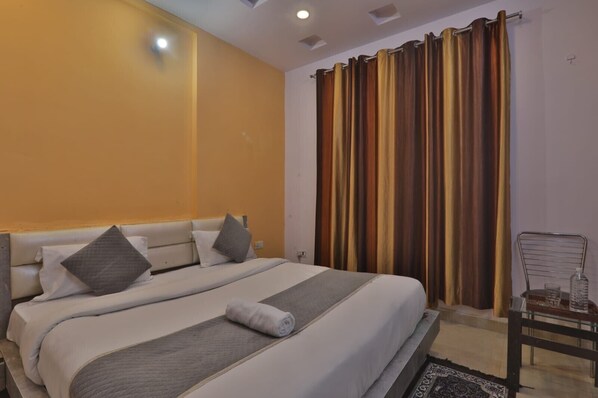 A hotel room with a large bed, a chair, and a window with curtains. - Hotel Shubhangi Inn (Lucknow)