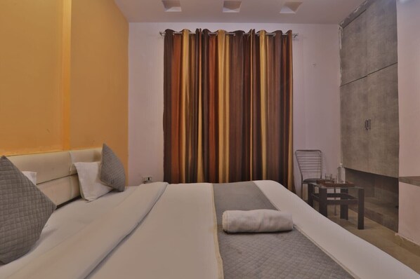 A bedroom with a bed, pillows, a chair, and a curtain. - Hotel Shubhangi Inn (Lucknow)