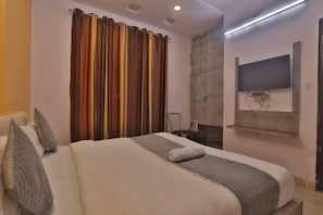 Ένα δωμάτιο ξενοδοχείου με ένα μεγάλο κρεβάτι, μια τηλεόραση επίπεδης οθόνης τοποθετημένη στον τοίχο και ένα παράθυρο με κουρτίνες.