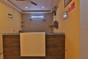 A reception area with a wooden reception desk, a ceiling fan, and a flat-screen TV mounted on the wall. - Hotel Shubhangi Inn (Lucknow)