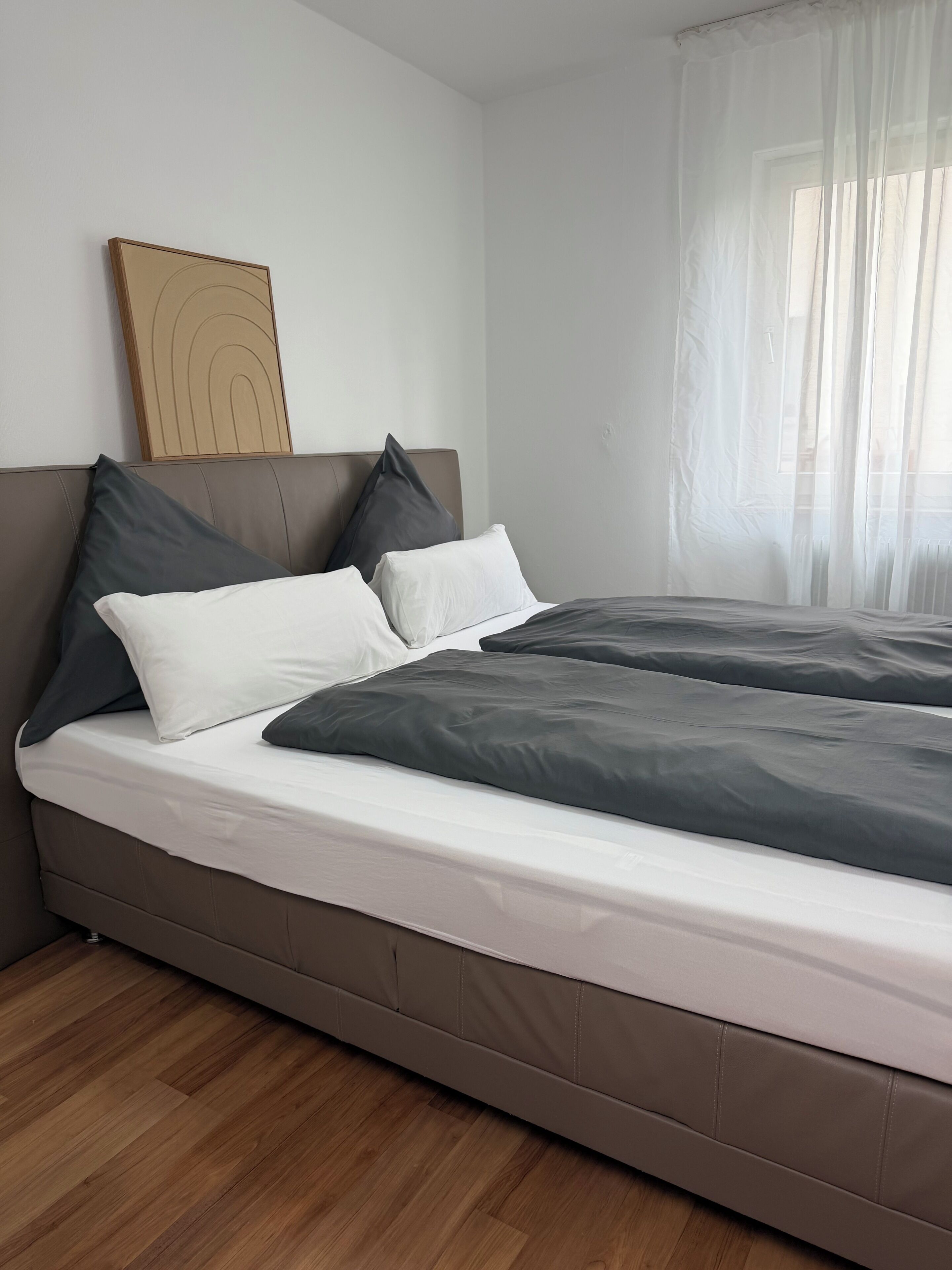Ein modernes Schlafzimmer mit einem großen Bett, einem Kopfteil mit dekorativer Zarge und Holzboden.