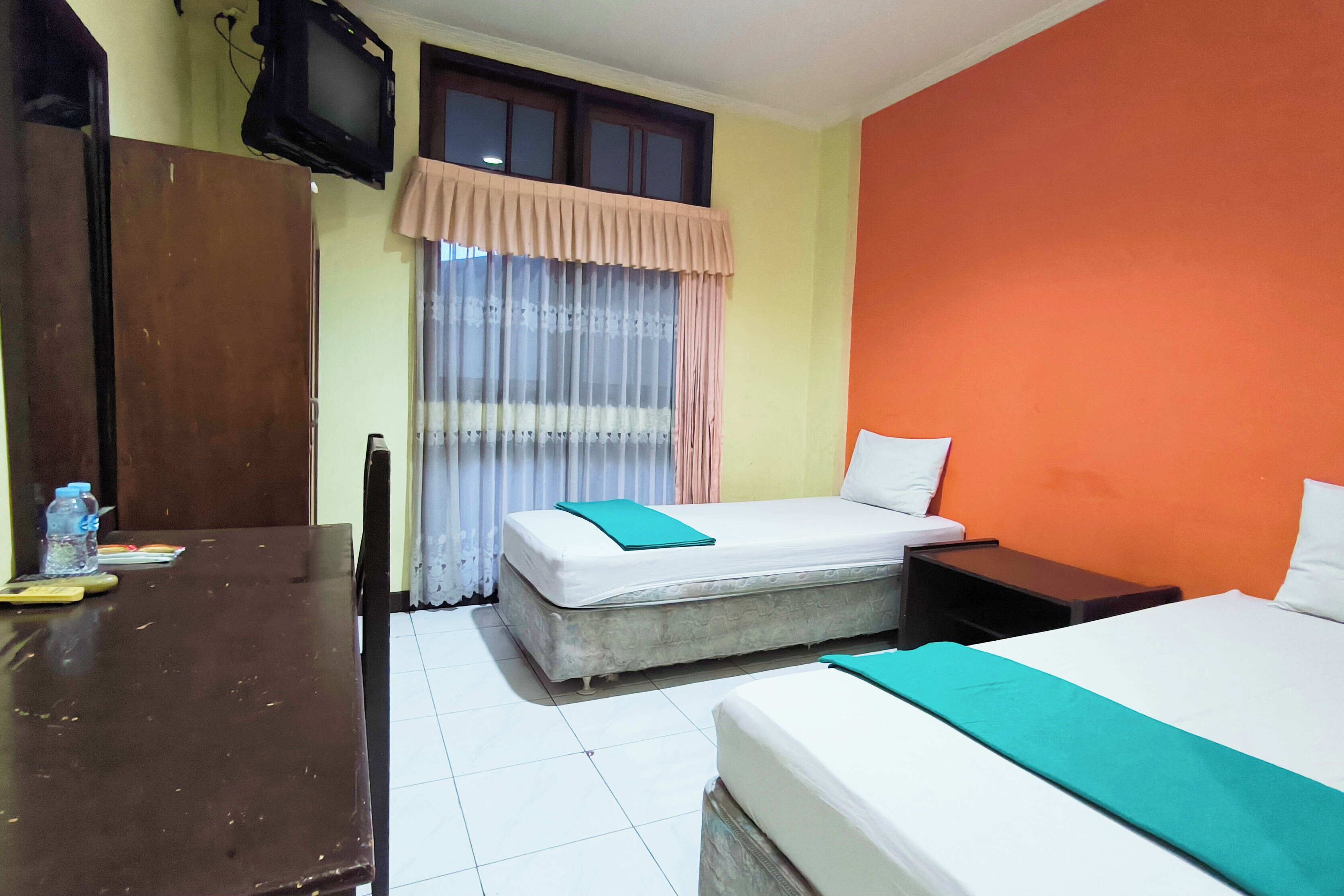 Habitación de hotel con dos camas, un televisor, una ventana con cortinas, una mesa con una botella de agua y una silla.