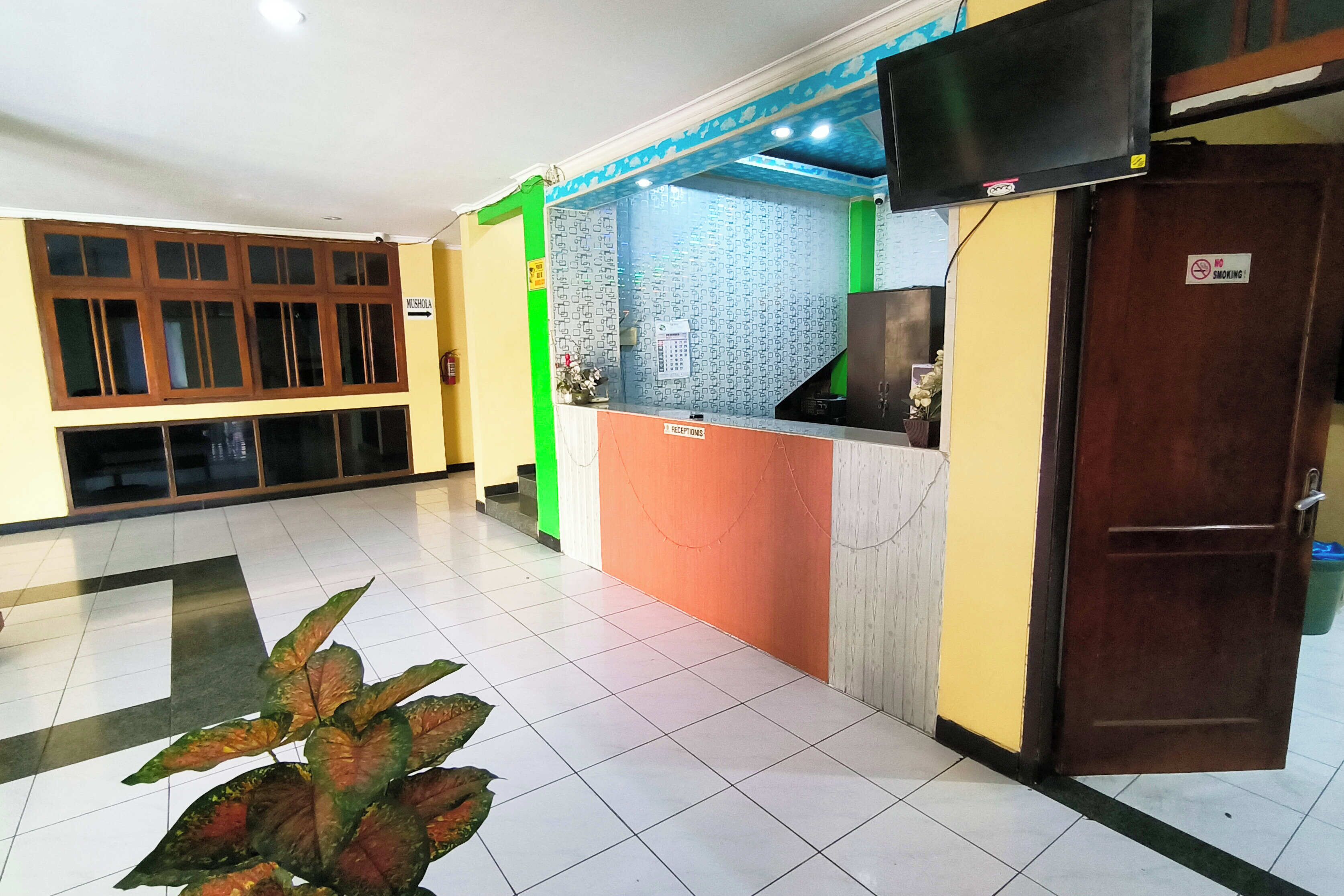 A hotel reception area with a reception desk, a television mounted on the wall, and a sign indicating a no-smoking area.