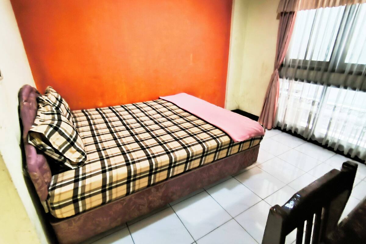 A small room with a bed, a chair, and a window with curtains.