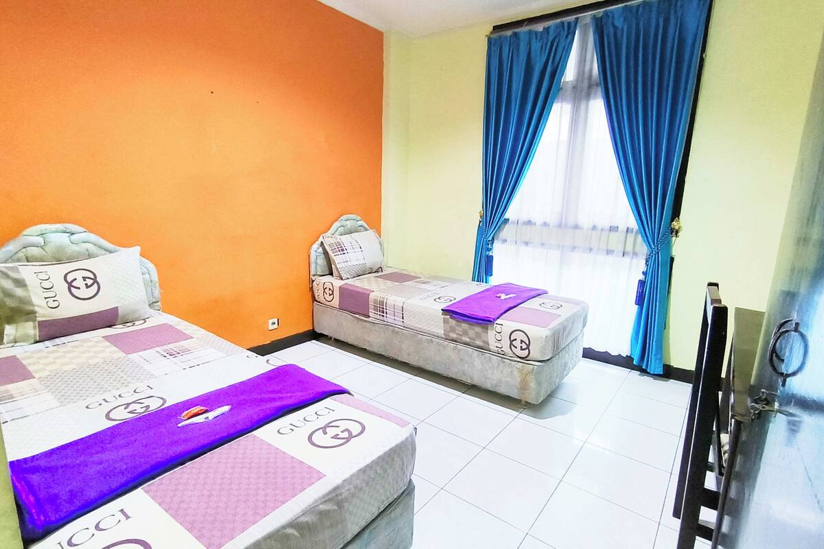 A hotel room with two beds, each with a Gucci blanket, a small sofa, and a TV.