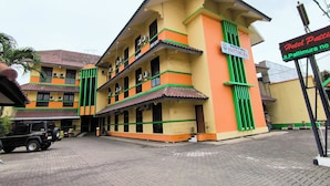 Ein mehrstöckiges Hotel mit gelber Fassade und grünen Akzenten, mit Balkonen und einem Schild, das Hotel Pattimura ausweist.