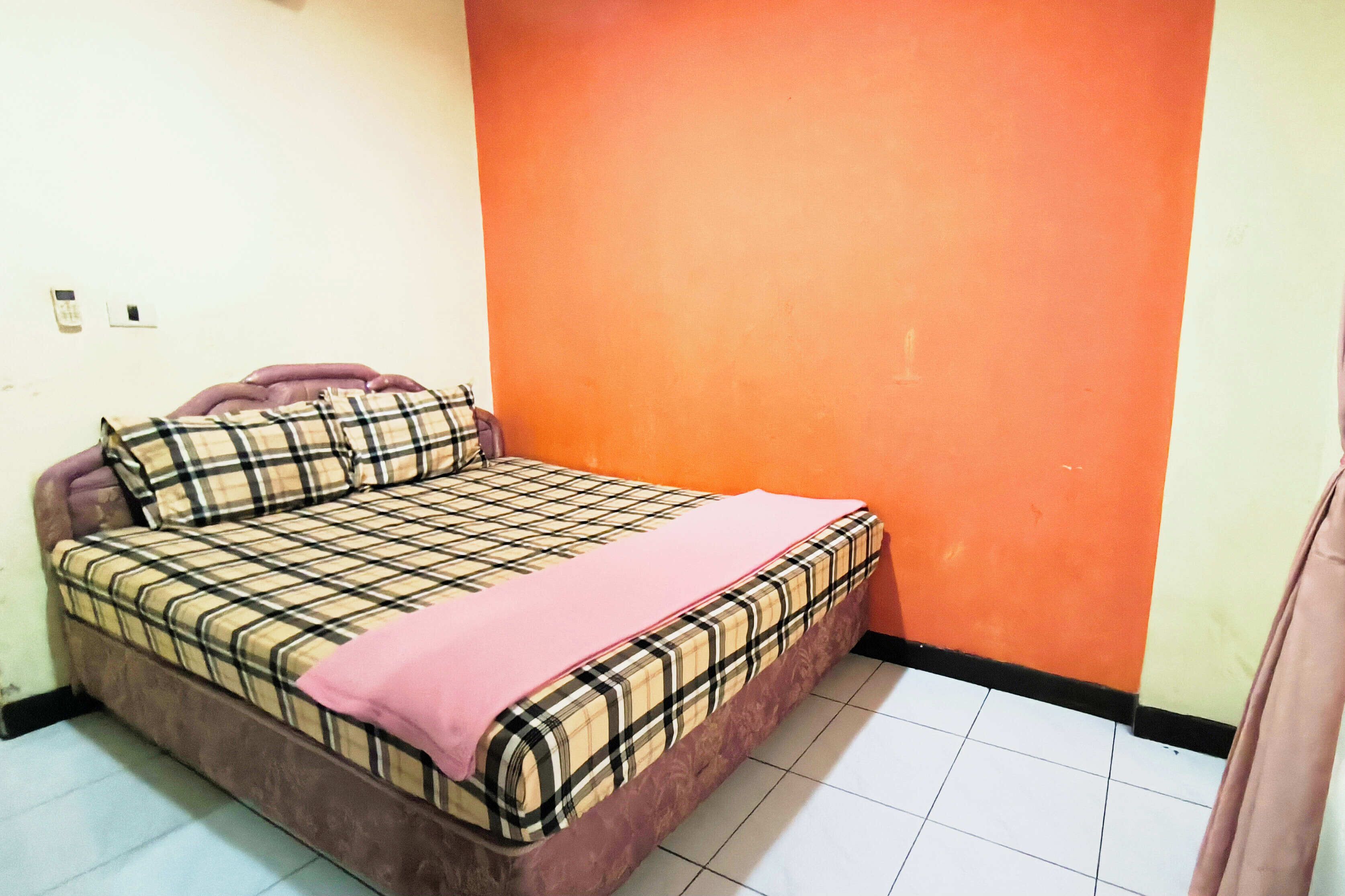 A single-bed room with a plaid bedspread, a pink blanket, and a brown headboard.