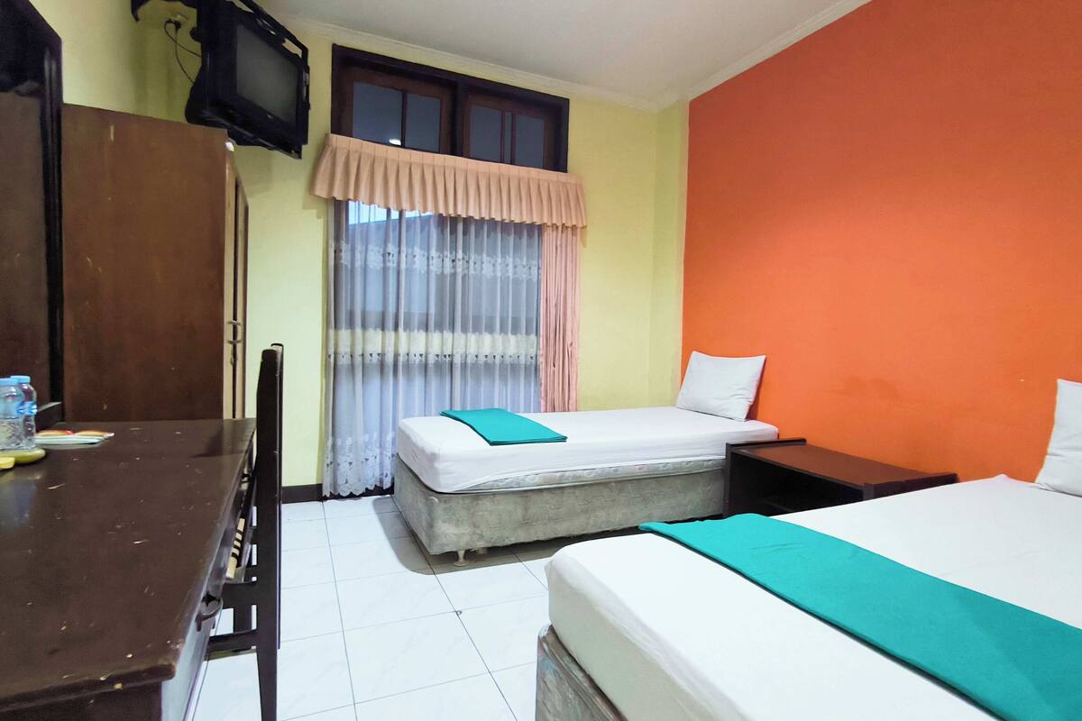 Una habitación con cama, escritorio, silla, televisor y ventana con cortinas.