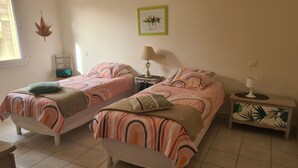 Une chambre avec deux lits, chacun agrémenté d’une couvre-lit et de coussins à motifs, une table de chevet avec une lampe, une petite table et un tableau accroché au mur.