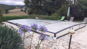 Un espace patio avec une table en verre, des sièges d’extérieur et une végétation luxuriante tout autour.