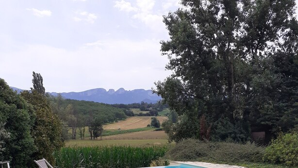 Une piscine dotée d’une plage en pierre, entourée de rochers et de plantes, et offrant une vue sur des collines lointaines.
