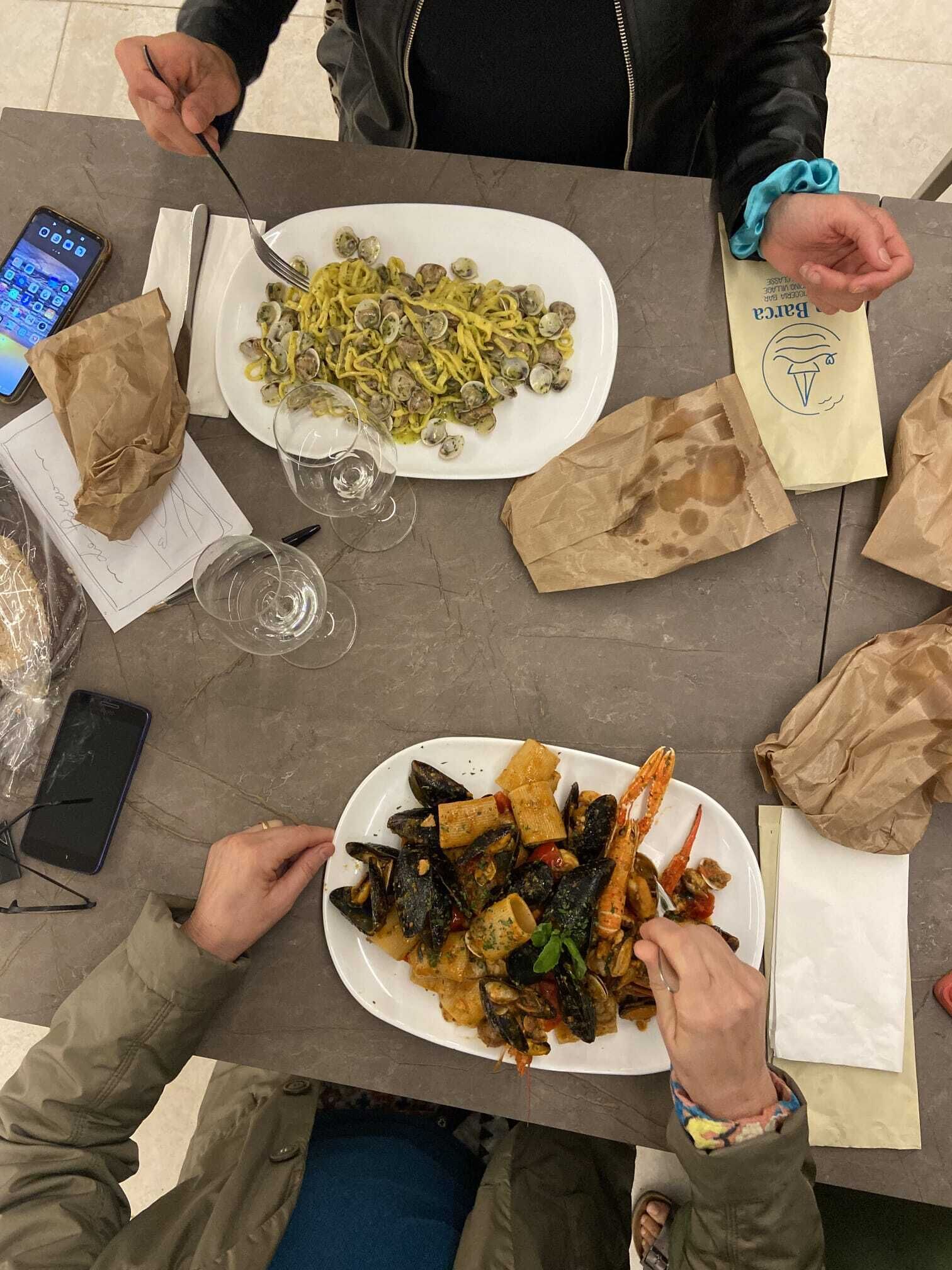 Une table à manger avec deux assiettes de pâtes et de fruits de mer, un téléphone intelligent et un sac en papier.