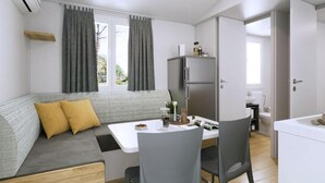 Ein gemütlicher, kompakter Wohnbereich mit Sofa, Esstisch, Stühlen, Kühlschrank und einer kleinen Küche.
