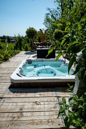 Un jacuzzi en una terraza de madera con un muro de piedra y follaje al fondo.