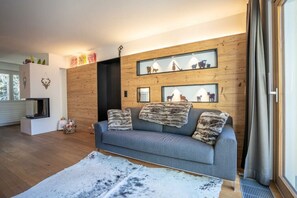 A modern living room with a grey sofa, wooden wall paneling, and framed animal prints. - St. Christoph by HomeFlow (Zermatt)