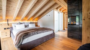 A bedroom with a large bed, wooden ceiling beams, and a fireplace. - Akelei Penthouse by HomeFlow Zermatt (Zermatt)
