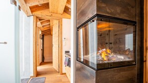 A modern kitchen with a large glass enclosure for a wood-burning stove, wooden beams on the ceiling, and a wooden floor. - Akelei Penthouse by HomeFlow Zermatt (Zermatt)