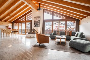 A spacious living area with a high ceiling and large windows, featuring a sofa, armchair, and dining table. - Turuwang Penthouse | HomeFlow Zermatt (Zermatt)