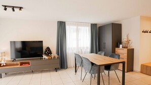 Un salon moderne avec un téléviseur à écran plat, une table à manger avec des chaises, un petit sapin de Noël et un meuble.