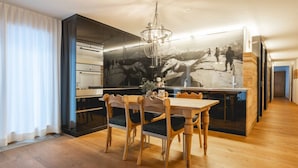 Ein moderner Essbereich mit Holztisch und -stühlen, einem großen Wandbild und einer Küche mit Edelstahlgeräten.