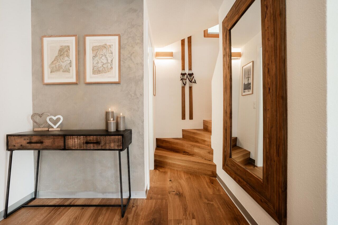 A hallway with a wooden desk, framed maps on the wall, and a wooden staircase.