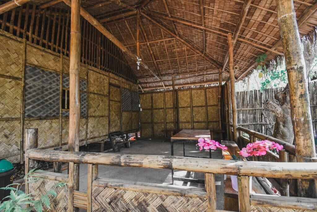 A bamboo hut with a thatched roof, a wooden table, and a bench.