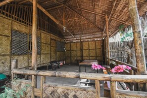 Uma cabana de bambu com telhado de palha, uma mesa de madeira e um banco.
