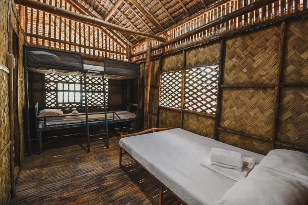 A room with a thatched roof, bamboo walls, a bunk bed, and a single bed.