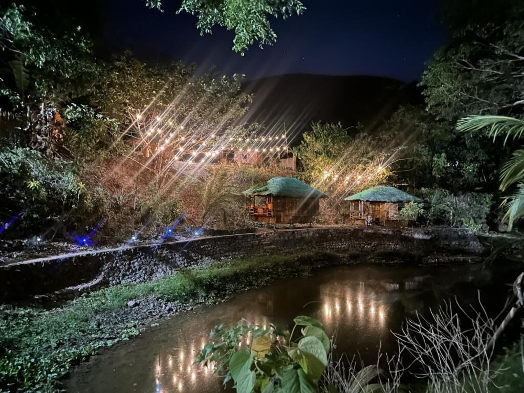 A nighttime view of a riverside area with illuminated structures and a bridge.