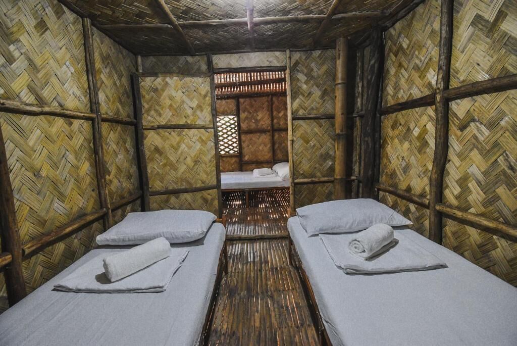 A room with two single beds, a wooden floor, and bamboo walls.