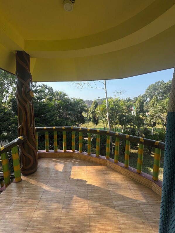 Une terrasse en bois dotée d’une balustrade incurvée, entourée d’une végétation luxuriante et d’arbres.